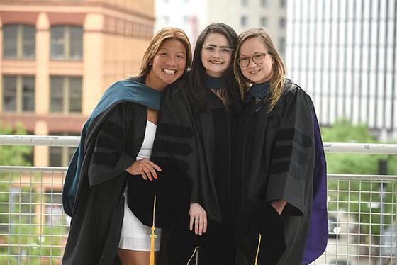 Three graduating students in robes pose outside and smile for a photo